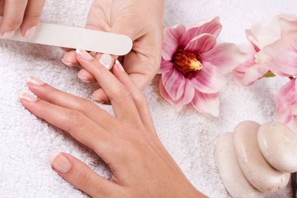 Person bekommt im Hotel Nagelpflege mit Feile auf weißem Handtuch.