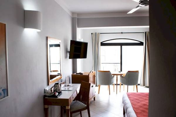 Innenansicht eines Hotelzimmers im Calypso Hotel mit Schreibtisch, Spiegel und Fernseher.