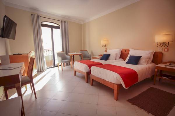 Doppelzimmer im Calypso Hotel mit zwei Betten, Schreibtisch, Stühlen und Fenstern.
