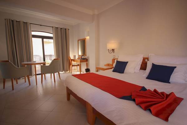 Innenansicht eines Hotelzimmers im Calypso Hotel mit einem Bett, Sesseln und einem Schreibtisch.
