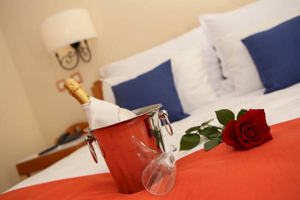Ein roter Weinkübel auf einem Bett mit einer roten Rose und einem Glas.