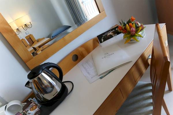 Ein Tisch im Hotelzimmer des Calypso Hotels mit einer Kaffeekanne, Papieren und einem Blumenstrauß.