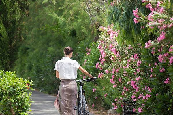 Frau mit Fahrrad am Cretan Malia Park entlang des Weges mit rosa Blumen