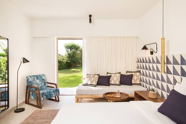 Innenansicht eines Zimmers im Cretan Malia Park Hotel mit weißem Bett, Sofa, Tisch und Dekoration.