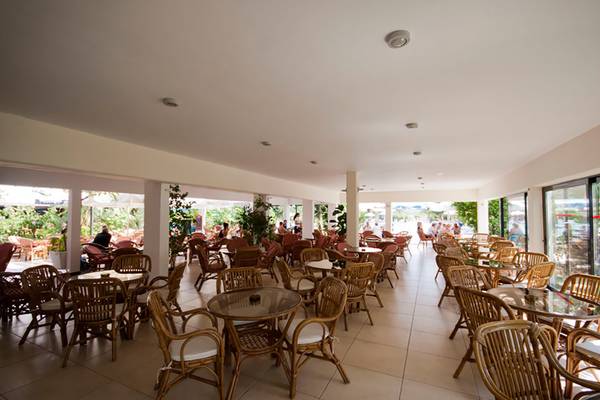 Innenbereich eines Hotels mit vielen Tischen und Stühlen, umgeben von Pflanzen und Glaswänden.