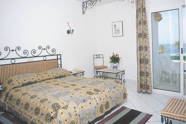 Schlafzimmer mit einem Bett, Tisch, Stuhl und Meerblick durch eine Glastür.