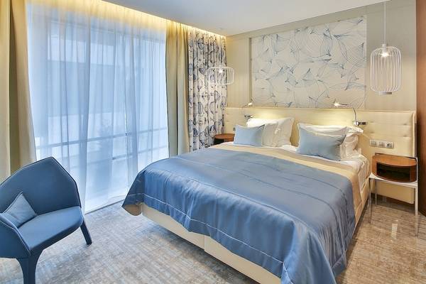 Schlafzimmer im Maritim Hotel Paradise Blue Albena mit einem großen Bett, blauen Laken und Kissen, neben einem Fenster mit Vorhängen.