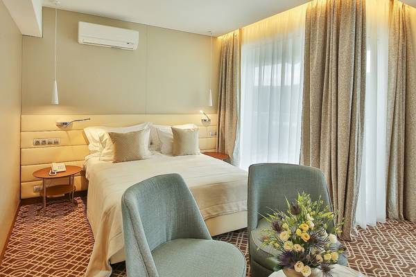 Ein elegantes Hotelzimmer im Maritim Hotel Paradise Blue Albena mit einem Bett, zwei Sesseln und einem Blumenstrauß.