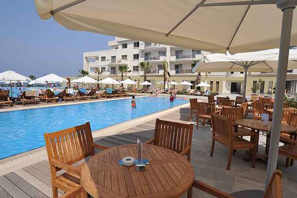 Pool-Terrasse des Capital Coast Resort & Spa mit Sonnenschirmen und Holzmöbeln.