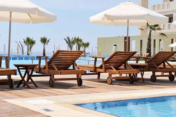 Holzliegen am Pool im Capital Coast Resort & Spa mit Sonnenschirmen und Blick auf das Meer.