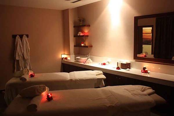 Zwei Massageliegen im Spa-Bereich des Capital Coast Resort & Spa mit weichen Laken, roten Kerzen und hängenden Handtüchern.