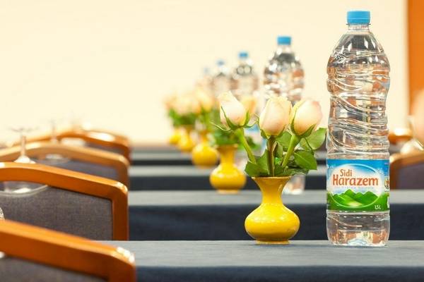 Konferenzraum im Le Meridien N'Fis Hotel mit blauen Tischen, weißen Rosen in gelben Vasen und Wasserflaschen.