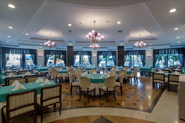 Innenansicht des Restaurants des Alba Queen Hotels mit runden Tischen und Stühlen, Kronleuchtern und Fenstern
