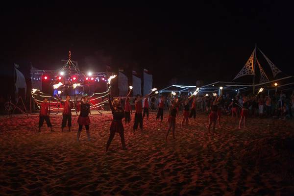 Nachtauftritt von Feuertänzern im Sand mit Fackeln und Publikum.