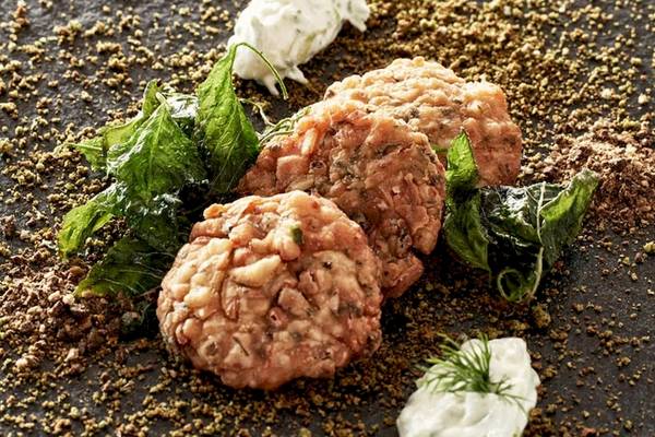 Fischkroketten von Myconian Kyma mit grünem Blattwerk und Gewürzen auf schwarzem Teller