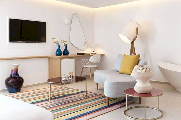 Innenansicht eines Zimmers im Myconian Kyma Hotel mit Badewanne, Fernseher, Couch und Tisch.