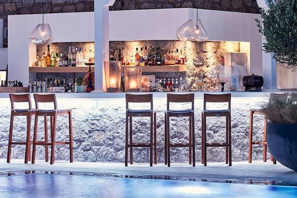 Außenbereich der Bar im Myconian Kyma Hotel mit Holzbarstühlen und einer großen Pflanze.