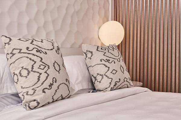 Bett im Myconian Kyma Hotel mit weißen Laken und gemusterten Kissen.