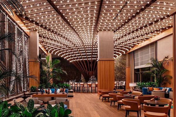 Interieur des Regnum Carya Golf & Spa Resorts mit beleuchteter Decke, Tischen und Stühlen, Pflanzen und Möbeln.