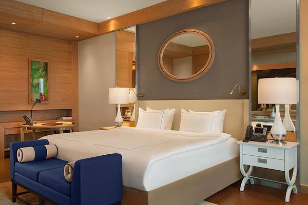 Hotelzimmer des Regnum Carya Golf & Spa Resorts mit großem Bett, blauem Sessel, Schreibtisch und Spiegel.