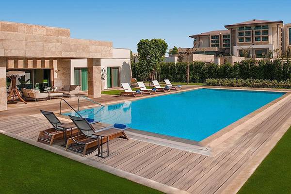 Außenpoolbereich des Regnum Carya Golf & Spa Resorts mit Lounge-Stühlen und Blick auf das Hotel
