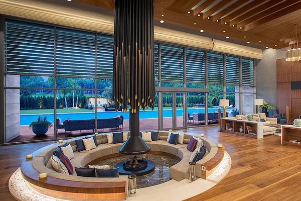 Wohnbereich des Regnum Carya Golf & Spa Resorts mit offenem Kamin, Couches und Panoramablick auf den Pool.