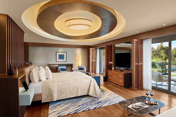 Interieur eines eleganten Schlafzimmers im Regnum Carya Golf & Spa Resort mit großem Bett, Balkon und Fernseher.