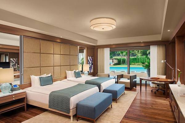 Schlafzimmer im Regnum Carya Golf & Spa Resort mit zwei Betten, Schreibtisch, Swimmingpool-Blick und moderner Einrichtung.