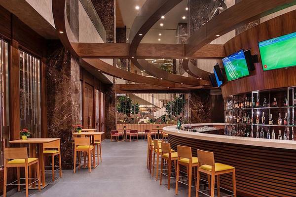 Innenansicht der Bar im Regnum Carya Golf & Spa Resort Hotel mit Holzmöbeln, Tischen und Stühlen.