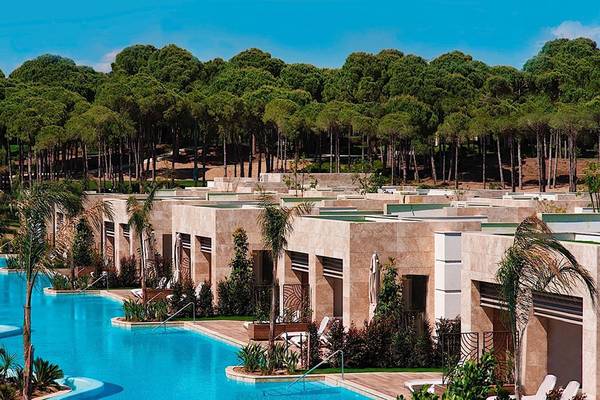 Außenansicht des Regnum Carya Golf & Spa Resorts mit Swimmingpool und umgebenden Bäumen.