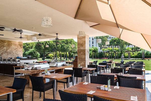 Regnum Carya Golf & Spa Resort Restaurant mit Außenbereich, Tischen, Stühlen und Sonnenschirmen.
