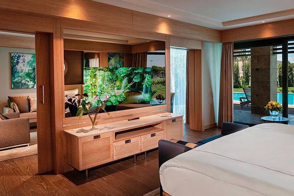 Suite-Innenansicht im Regnum Carya Golf & Spa Resort mit großem Fernseher und Poolblick.