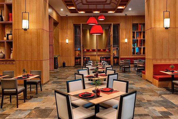 Innenansicht des Restaurants im Regnum Carya Golf & Spa Resort mit Holzelementen, roten Leuchten und gefliestem Boden.
