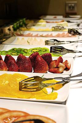 Buffet mit verschiedenen Obstsalaten und Früchten wie Erdbeeren, Kiwis und Orangen.