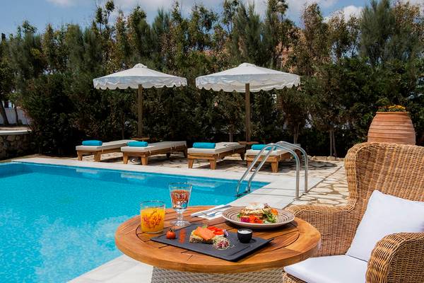 Poolbereich im Mitsis Blue Domes Resort & Spa mit Sonnenliegen und Frühstückstisch.