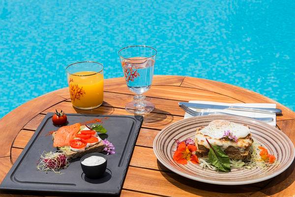Frühstück am Pool im Mitsis Blue Domes Resort & Spa mit zwei Tellern, Orangensaft und Wasser.