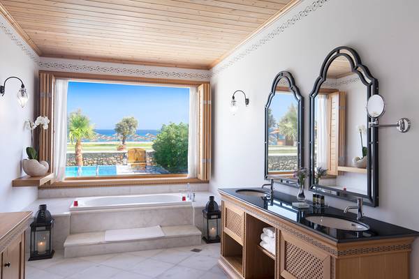 Badezimmer des Mitsis Blue Domes Resort & Spa mit Aussicht auf den Pool und das Meer.