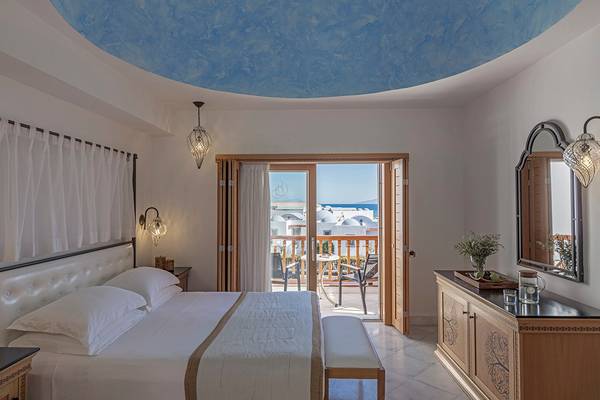 Schlafzimmer im Mitsis Blue Domes Resort & Spa mit Blick auf den Balkon und das Meer.