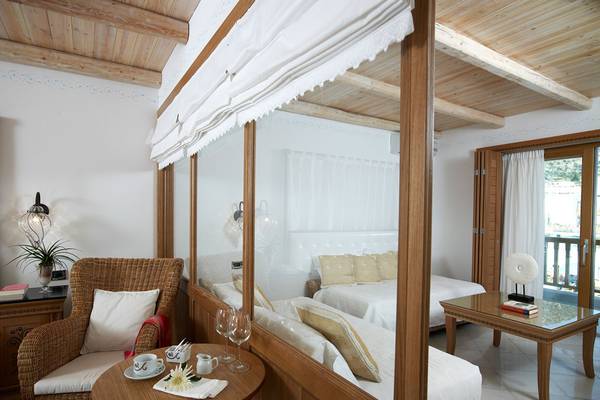 Innenansicht eines Schlafzimmers im Mitsis Blue Domes Resort & Spa mit einem Bett, einem Tisch, einem Stuhl und einem Glasfenster.