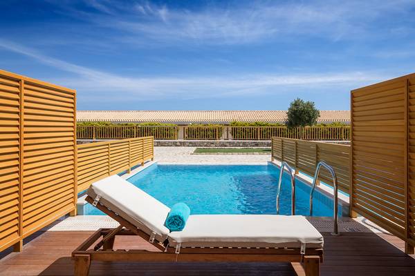 Eine Holzliege mit einem blauen Handtuch neben einem Pool im Mitsis Blue Domes Resort.