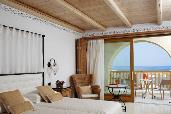 Schlafzimmer im Mitsis Blue Domes Resort & Spa mit Meerblick, inklusive Doppelbett, Sessel, Nachttisch und Balkon mit Tisch und Stühlen.