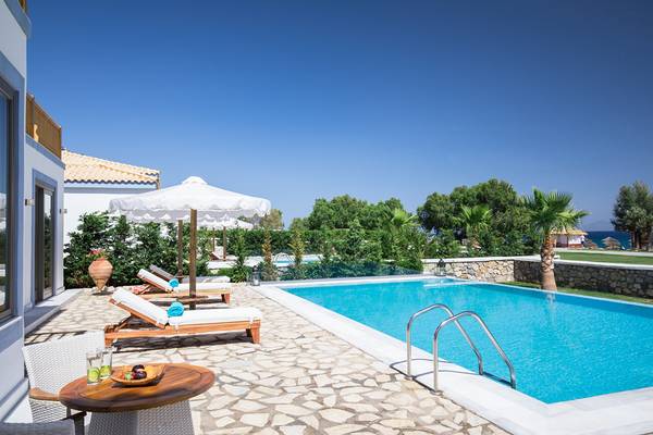 Außenpoolbereich des Mitsis Blue Domes Resorts & Spa mit Loungeliegen und einem Tisch
