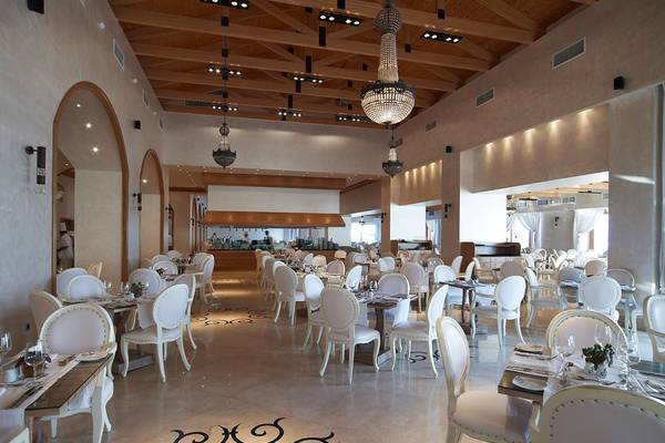 Restaurant des Mitsis Blue Domes Resort & Spa mit weißen Stühlen und Tischen, Holzdecken und Kronleuchtern.