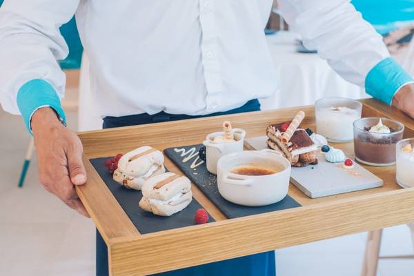 Ein Kellner serviert eine Holztablett mit verschiedenen Desserts und Speisen im Iberostar Selection Playa de Palma Hotel.
