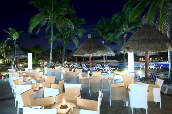 Terrasse des Bahia Principe Grand Tulum Hotels bei Nacht mit vielen Stühlen und Tischen unter Palmen.