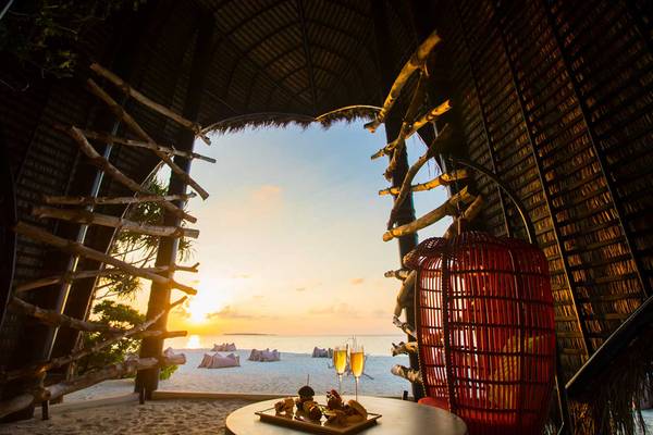 Abendstrand-Szene im Dhigali Maldives mit Blick auf den Sonnenuntergang und einem Tisch mit Getränken und Speisen.