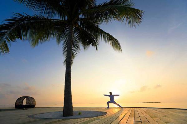 Yoga auf dem Holzdeck am Strand im Dhigali Maldives bei Sonnenuntergang.