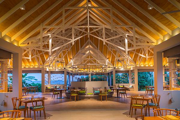 Innenbereich des Dhigali Maldives Hotels mit offenem Dach, Tischen und Stühlen.