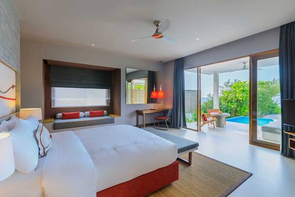Innenansicht eines Hotelzimmers im Dhigali Maldives Hotel mit großem Bett, Sofa und Poolblick.