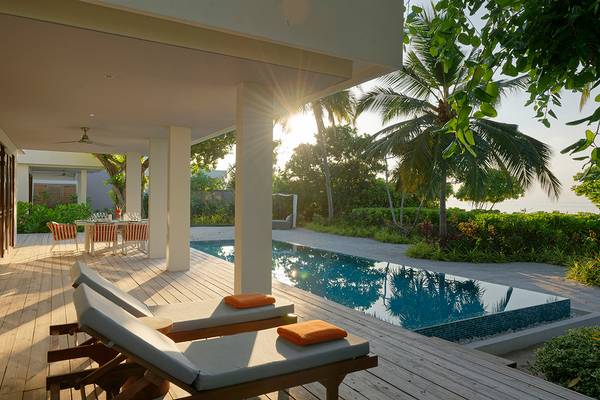 Außenbereich des Dhigali Maldives Hotels mit Pool, Loungeliegen und Esstisch.